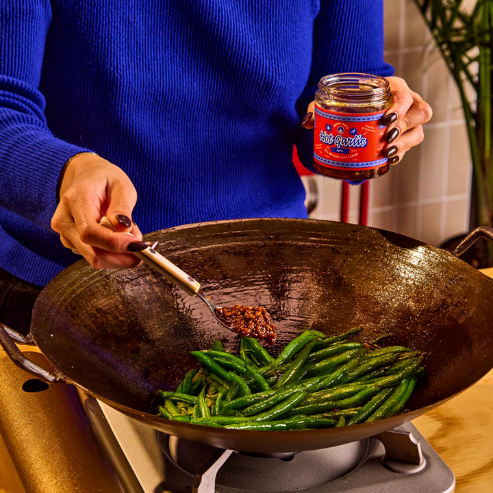 Person cooking green beans in a wok with a jar of sauce in the background