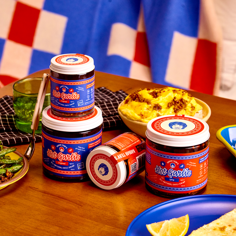 Jars of 'Hot Garlic' sauce on a table with food in the background