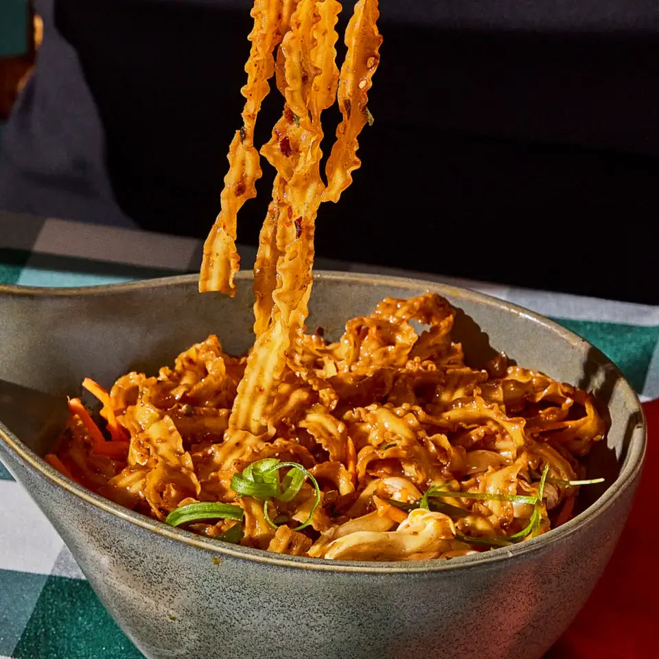 Bowl of noodles with a focus on the noodles being lifted, set against a dark background.