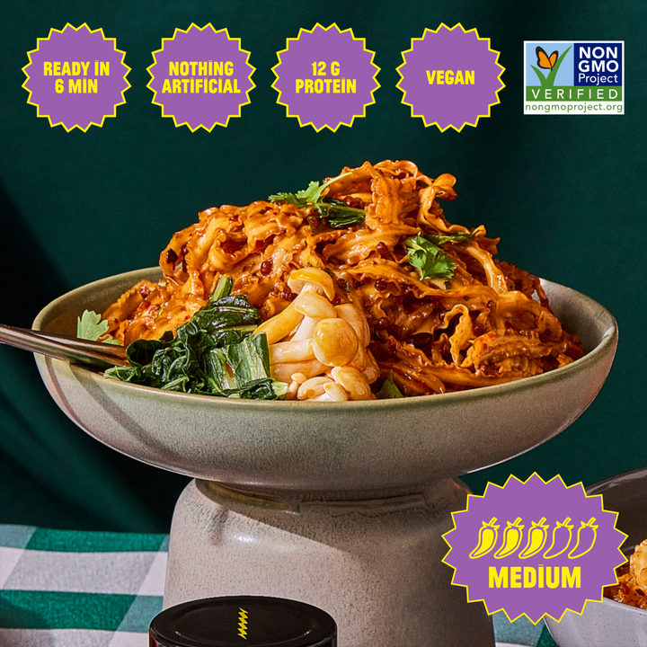 Bowl of pasta with toppings on a stand against a dark background, featuring nutritional and certification labels.
