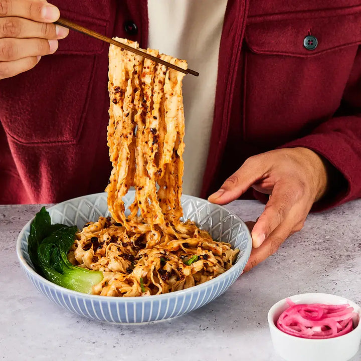 Person lifting noodles with chopsticks from a bowl on a table.