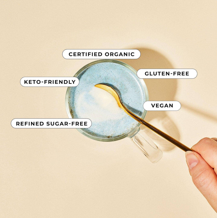 Glass mug with a spoonful of a product, labeled as certified organic, gluten-free, keto-friendly, refined sugar-free, and vegan on a beige background.