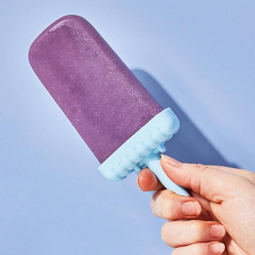 Purple popsicle with a blue stick held by a hand against a light purple background