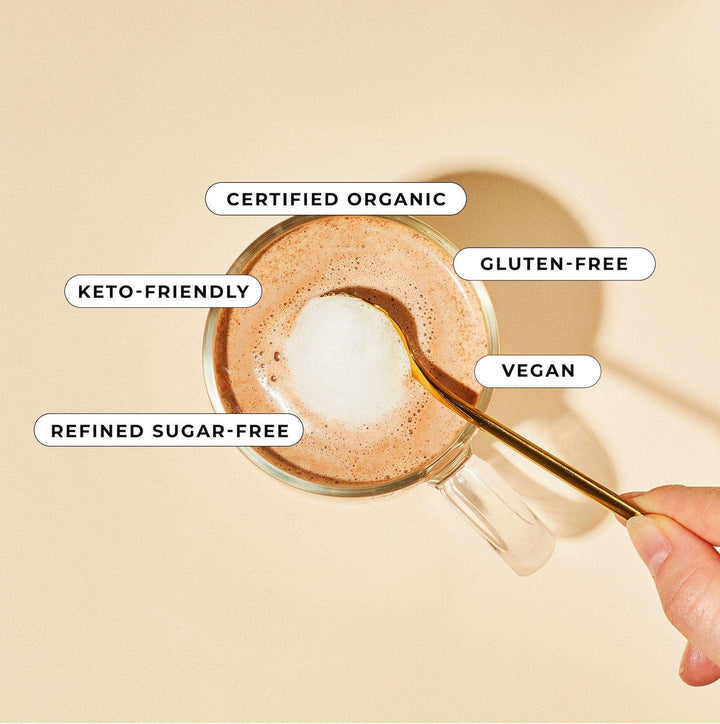 Glass of coffee with a spoon, labeled as certified organic, gluten-free, keto-friendly, refined sugar-free, and vegan on a beige background.