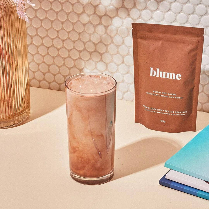 Glass of hot chocolate and a package of blume hot chocolate on a table with a decorative background.