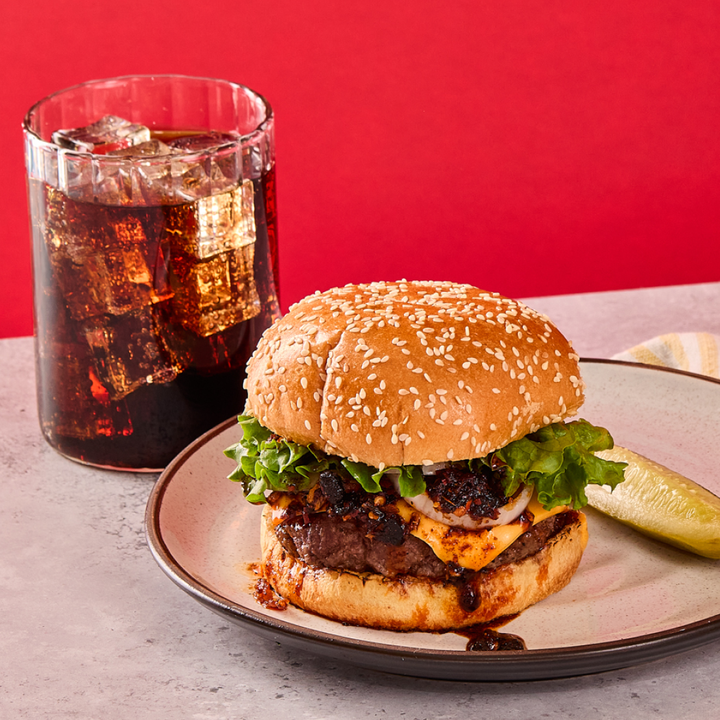 Hamburger with a side of cola on a plate against a red background
