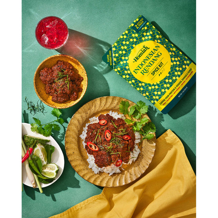 Indonesian Rendang dish with ingredients and a spice kit on a green background