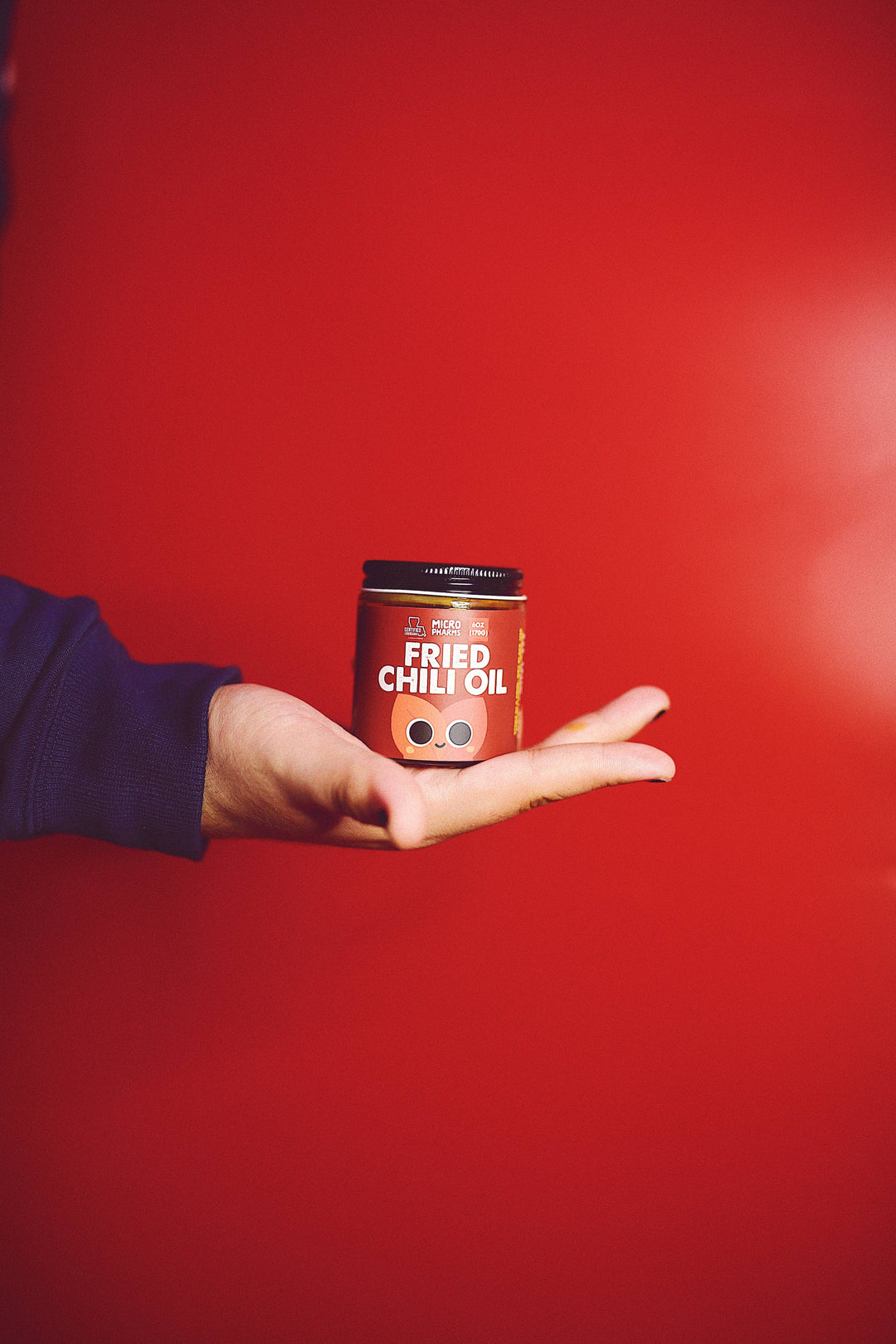 A hand holding a small jar of Fried Chili Oil against a solid red background.