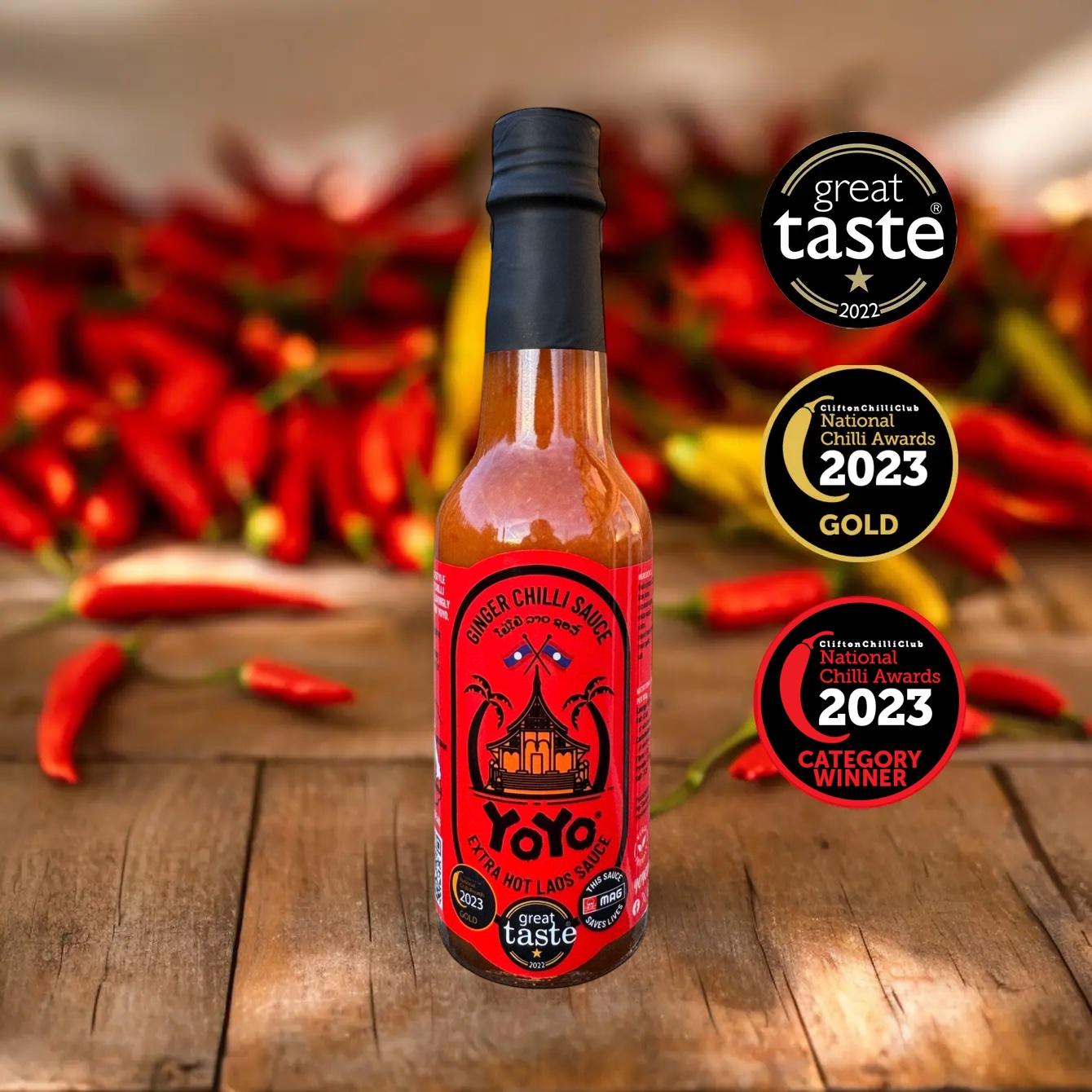 Bottle of Yoyo Chilli Sauce with awards on a wooden surface with red chillies in the background