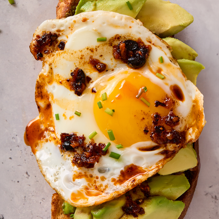 Fried egg on toast with avocado slices on a gray surface