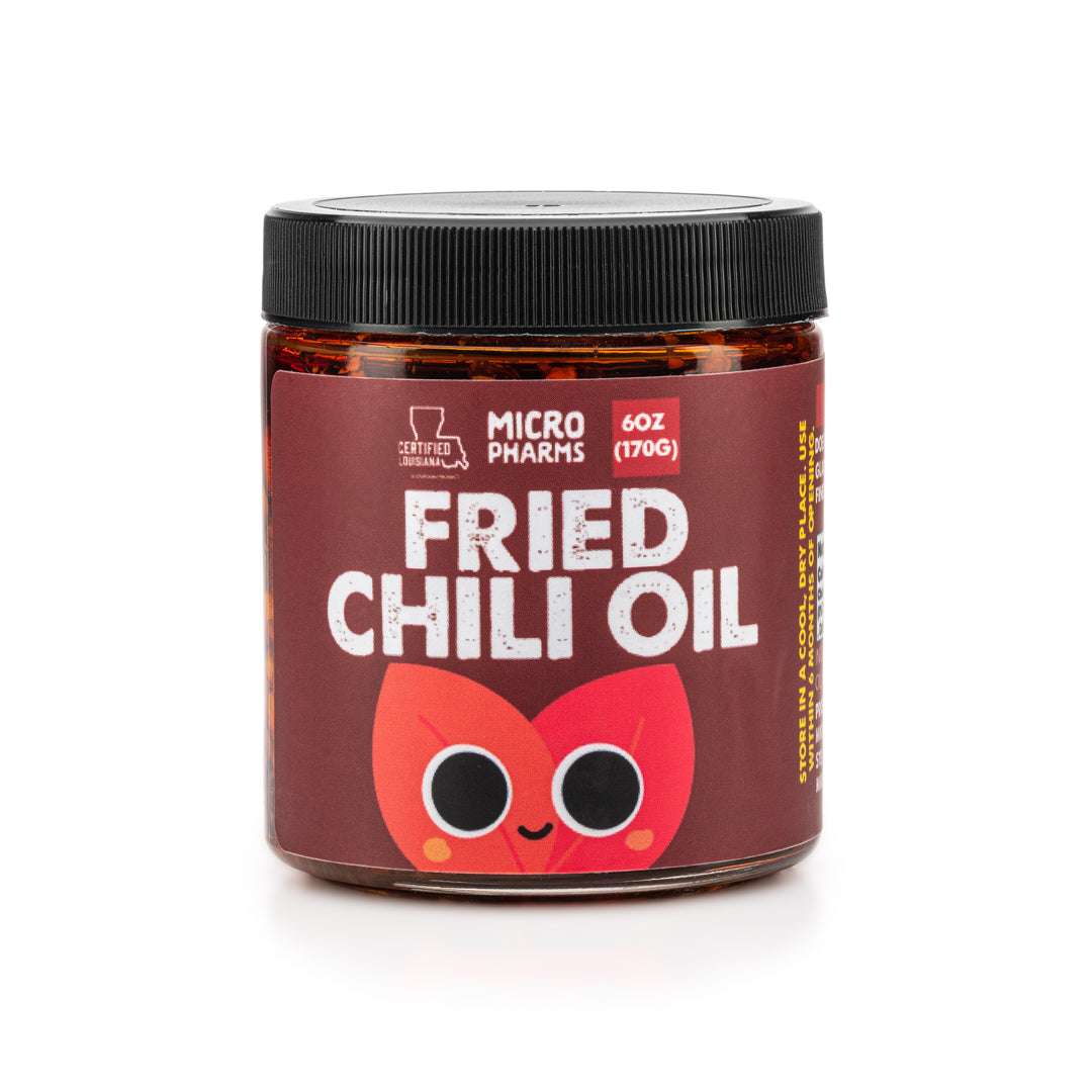 A jar of Micro Pharms Fried Chili Oil with a label featuring a cartoon chili pepper. The jar is brown with a black lid and the product weight is indicated as 6 oz (180g).